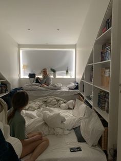 two people are sitting on their beds in a room with bookshelves and shelving