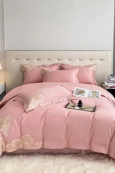 a bed with pink comforter and pillows in a room next to a lamp on a table