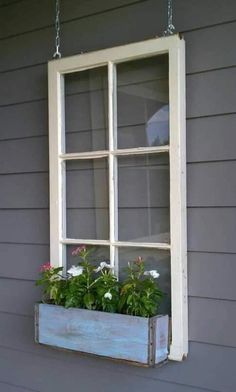 an old window is hung on the side of a gray house with flowers in it