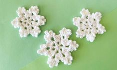 two crocheted snowflakes sitting on top of a green surface