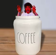 a white coffee jar with the word coffee painted on it's front and hands in the air