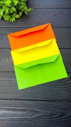 an orange, yellow and green envelope sitting on top of a wooden table next to a plant