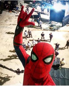 a spider - man is standing in front of a group of people with their hands up