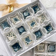 an open box filled with decorative blue and white cookies on top of a table next to a gold ribbon