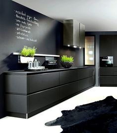 a black and white kitchen with chalkboard on the wall above the countertop, potted plants in vases next to it