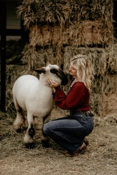 a woman kneeling down petting a sheep on top of dry grass and straw bales