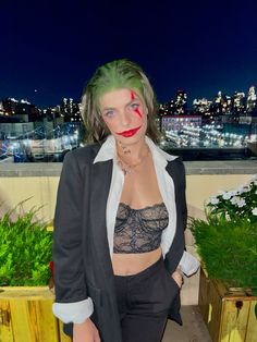 a woman with green hair and makeup is posing for the camera in front of a cityscape