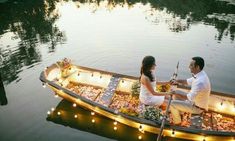 a man and woman sitting in a boat with food on the water at night time