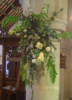 a tall white pillar with flowers and greenery hanging from it's sides in a church