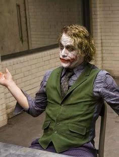 a man dressed as the joker sitting at a table with his hands in the air