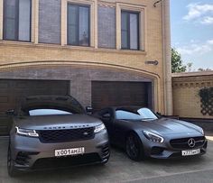 two cars parked next to each other in front of a large brick building with garage doors