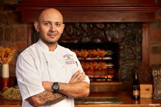 a chef standing in front of a fireplace with his arms crossed