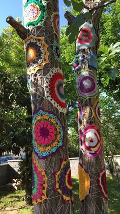 two wooden poles with crocheted designs on them and trees in the back ground