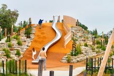 two people are standing at the top of a hill with a slide in front of them