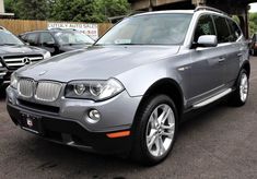 a silver bmw suv parked in a parking lot next to other cars and people looking at it