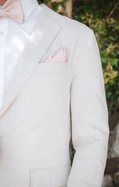 a man in a white suit with a pink bow tie and pocket square on his lapel