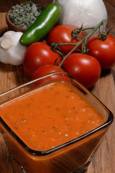 tomatoes, onions, garlic and peppers on a cutting board next to a bowl of tomato sauce