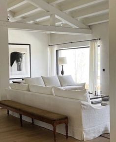 a large white couch sitting in a living room next to a wooden table and window