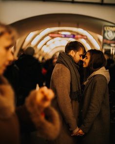 a man and woman standing in front of a train station with their arms around each other