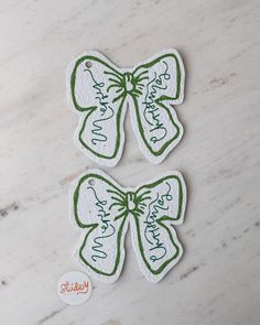 two green and white bows with words on them sitting on a marble counter top next to a sticker