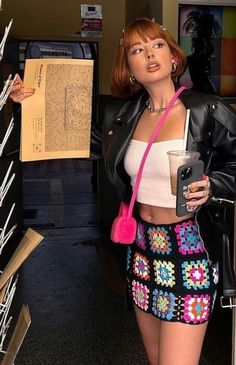 a woman standing next to a shelf holding a cell phone and wearing a pink purse