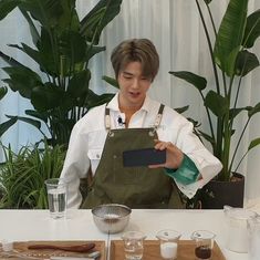 a man in an apron holding up a cell phone at a table with utensils