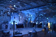 a room filled with tables and chairs covered in white paper lanterns hanging from the ceiling