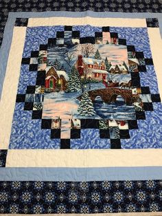 a quilted table topper with a winter scene on it's side and houses in the background