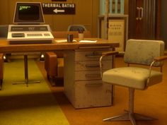 an old computer sitting on top of a wooden desk next to a filing cabinet and chair