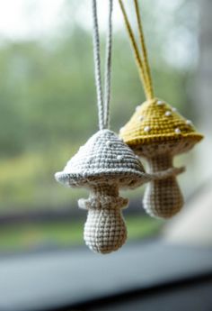 two crocheted mushrooms hanging from strings on a window sill