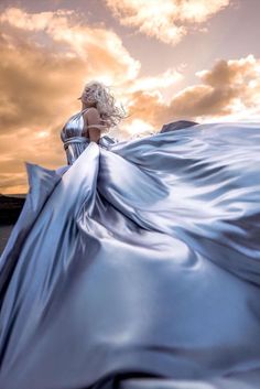 a woman in a long blue dress is standing on the beach with her back to the camera