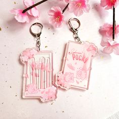 two keychains with pink flowers on them next to a flower pot and card