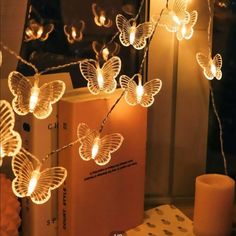 the butterfly string lights are on display in front of an open book and lit candle