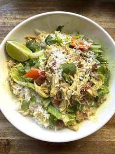 a white bowl filled with rice, meat and veggies on top of a wooden table