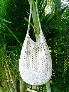 a white crocheted purse hanging from a palm tree