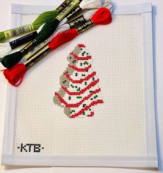 a cross stitch christmas tree with red and green tassels next to two crochet hooks