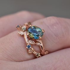 a close up of a person's hand holding a ring with a blue and green stone