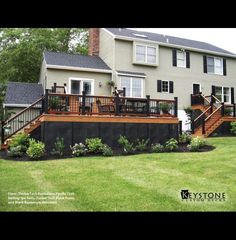 a large house with a deck in front of it and landscaping around the back yard