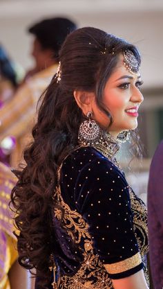 a woman with long hair wearing a black and gold dress standing in front of other people