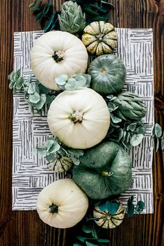 some white pumpkins and green leaves on a wooden table with a cloth place mat