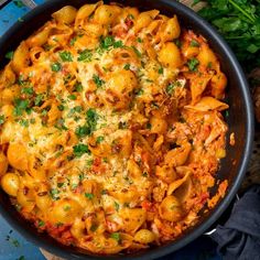 a skillet filled with pasta and sauce on top of a wooden table next to parsley