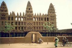 two people on bicycles are standing in front of an adobe - style building with intricately carved windows