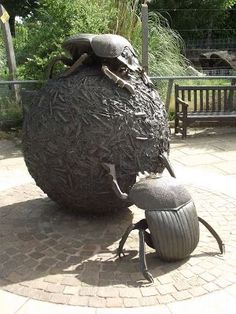 a statue of a bug crawling in front of a large ball with its head on it's back