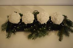 some white flowers and greenery on a shelf with lights in the corner behind them