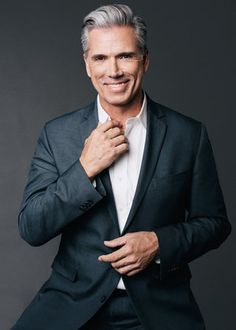 a man in a black suit and white shirt is posing for a photo with his hands on his chest