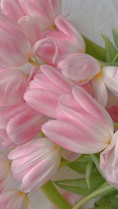 a bouquet of pink tulips sitting on top of a white table cloth with green stems