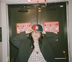 a woman wearing a hat and glasses standing in front of two emergency exit only signs