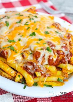 a white plate topped with cheesy french fries covered in cheese and sauce on top of a checkered table cloth