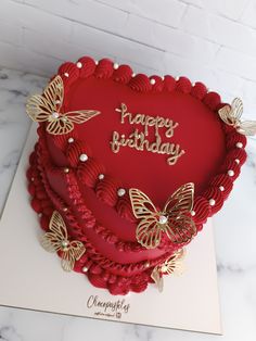 a red heart shaped cake with gold butterflies on it's side and the words happy birthday written on top