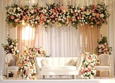 a white couch sitting under a flower covered arch on top of a table next to two chairs